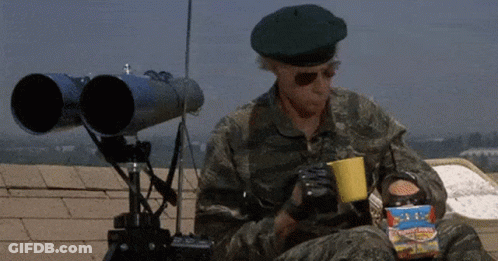 A Man In A Military Uniform Is Sitting On A Roof Holding A Cup Of Coffee And A Box Of Popcorn . GIF
