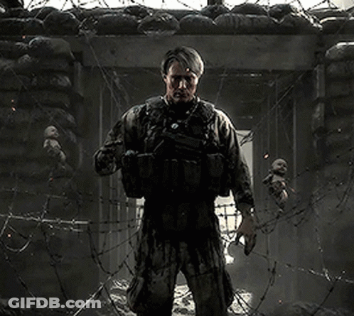 A Man In A Military Uniform Is Standing In Front Of A Barbed Wire Fence Holding A Baby . GIF