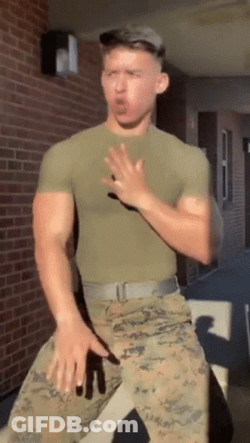 A Man In A Military Uniform Is Standing In Front Of A Brick Building Making A Funny Face . GIF