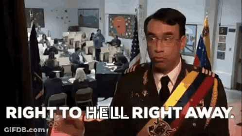 A Man In A Military Uniform Is Standing In Front Of A Room With People Sitting At Desks And Flags . GIF