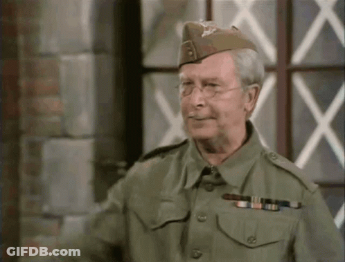 A Man In A Military Uniform Is Standing In Front Of A Window And Smiling GIF
