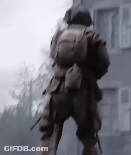 A Man In A Military Uniform Is Walking In Front Of A Building With A Backpack On His Back . GIF