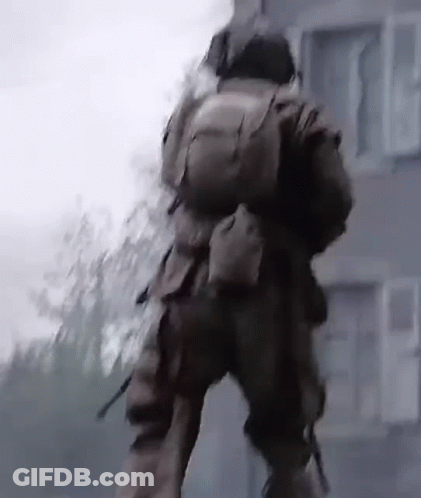 A Man In A Military Uniform Is Walking In Front Of A Building With A Backpack On His Back . GIF