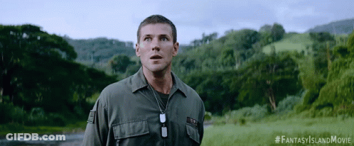 A Man In A Military Uniform Stands In A Field With Trees In The Background And A #Fantasyislandmovie Hashtag GIF