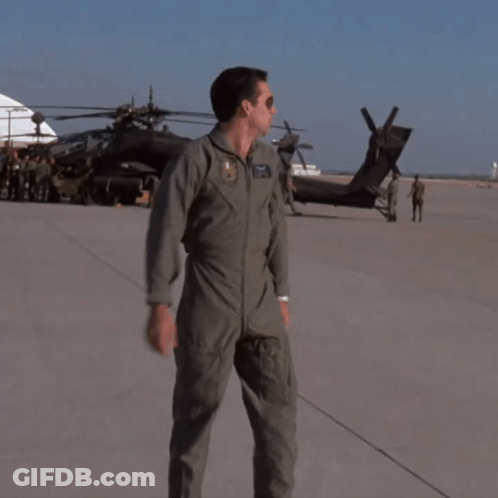 A Man In A Military Uniform Stands On A Runway In Front Of A Black Helicopter GIF