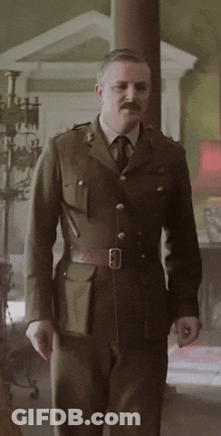 A Man In A Military Uniform With A Mustache Is Standing In A Room GIF