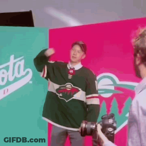 A Man In A Minnesota Wild Jersey Is Being Photographed By A Cameraman . GIF