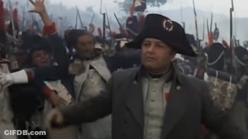 A Man In A Napoleon Hat Stands In Front Of A Crowd GIF