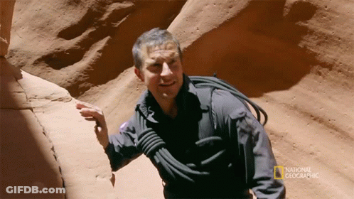 A Man In A National Geographic Shirt Is Standing In A Canyon GIF