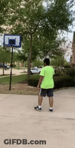 A Man In A Neon Green Shirt Is Playing Basketball On A Sidewalk GIF