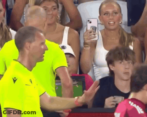 A Man In A Neon Green Shirt Is Talking To Another Man In A Crowd GIF