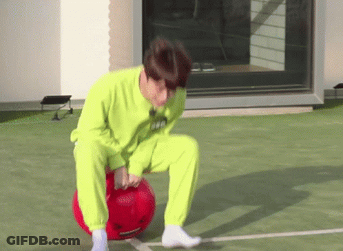 A Man In A Neon Green Sweater Is Kneeling On A Red Ball . GIF