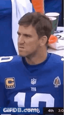 A Man In A New York Giants Jersey Is Sitting At A Table And Making A Funny Face . GIF