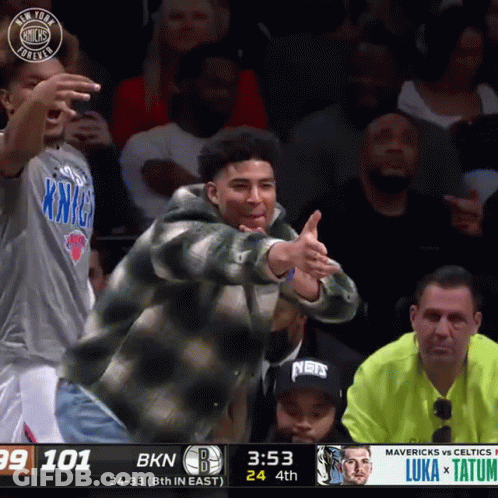 A Man In A New York Knicks Shirt Is Giving A Thumbs Up During A Basketball Game GIF