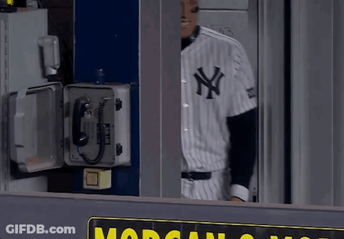 A Man In A New York Yankees Uniform Stands In Front Of A Phone Box GIF