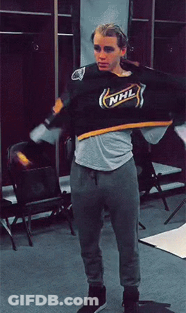 A Man In A Nhl Jersey Is Standing In A Room GIF