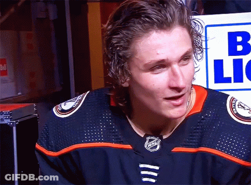 A Man In A Nhl Jersey Stands In Front Of A Sign That Says B Lic GIF