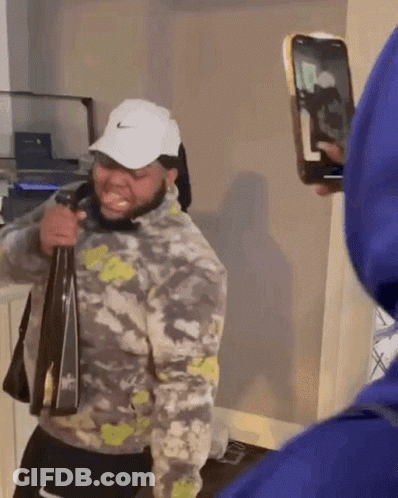A Man In A Nike Hat Is Holding A Bag And Taking A Picture Of Himself With A Phone . GIF