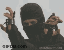 A Man In A Ninja Mask Is Holding A Gun In His Hand GIF