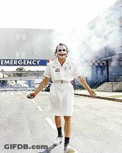 A Man In A Nurse Costume Is Walking Down A Street In Front Of An Emergency Sign GIF