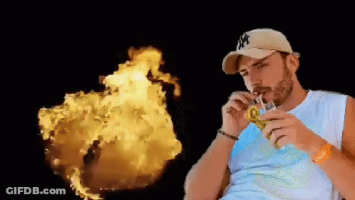 A Man In A Ny Hat Is Drinking Through A Straw In Front Of A Fireball . GIF