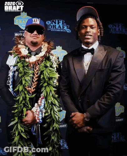 A Man In A Ny Hat Stands Next To A Man In A Suit GIF