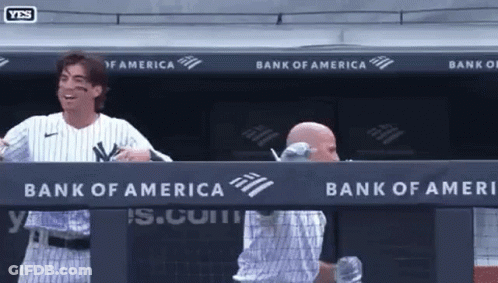 A Man In A Ny Yankees Uniform Stands In A Dugout With A Bank Of America Banner Behind Him GIF
