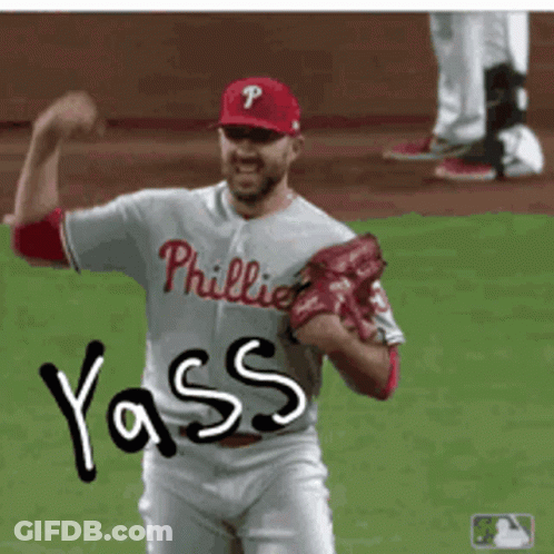 A Man In A Phillies Jersey Is Flexing His Muscles On A Baseball Field GIF