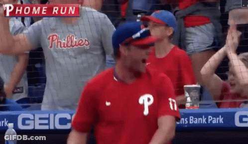 A Man In A Phillies Shirt Is Standing In The Stands GIF