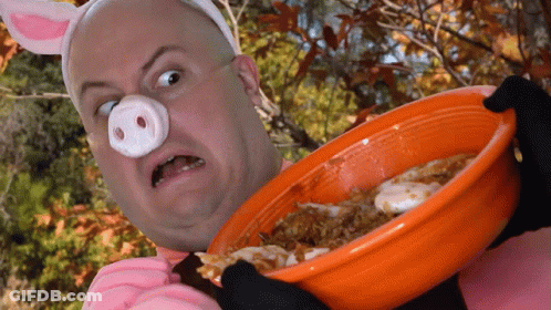 A Man In A Pig Costume Is Holding An Orange Bowl Of Food GIF