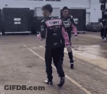 A Man In A Pink And Black Racing Suit Is Walking Down A Sidewalk . GIF