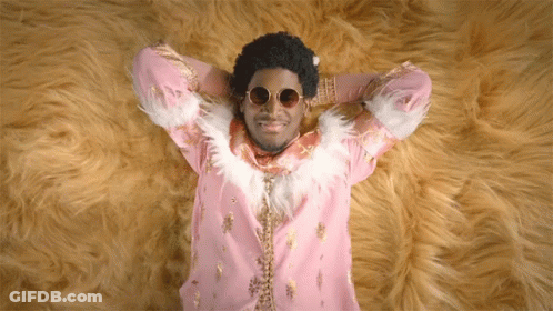 A Man In A Pink And Gold Outfit Is Laying On A Furry Rug GIF
