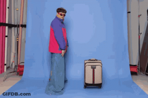 A Man In A Pink And Purple Jacket Is Standing Next To A Suitcase GIF
