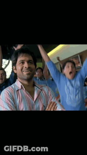 A Man In A Pink And White Striped Shirt Stands In Front Of A Crowd GIF