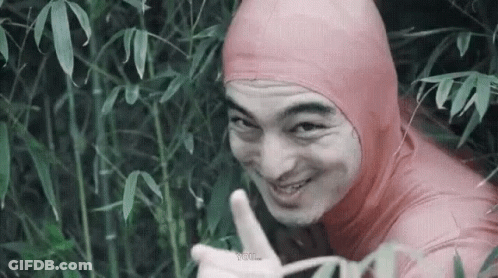 A Man In A Pink Bodysuit Is Giving A Thumbs Up While Standing In A Forest . GIF