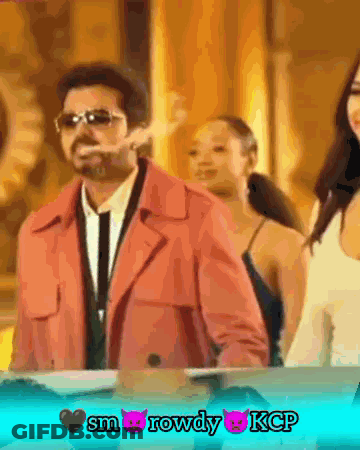 A Man In A Pink Coat Is Smoking A Cigarette In Front Of Two Women GIF