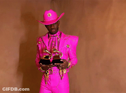 A Man In A Pink Cowboy Hat Is Holding A Pair Of Grammys GIF