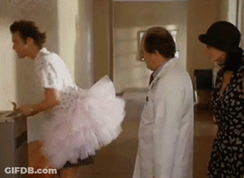 A Man In A Pink Dress Is Standing Next To A Doctor And A Woman In A Hat . GIF