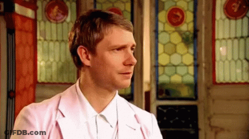 A Man In A Pink Jacket And White Shirt Is Standing In Front Of A Stained Glass Door . GIF