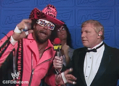 A Man In A Pink Jacket Is Holding A Microphone While Talking To Two Men In Tuxedos . GIF