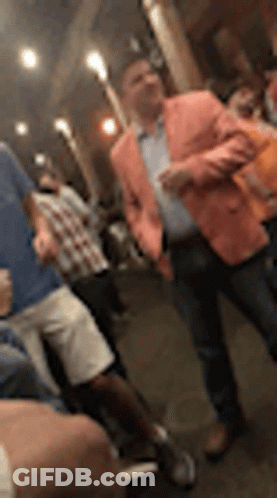 A Man In A Pink Jacket Is Standing In A Crowd Of People At A Party . GIF