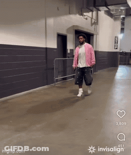 A Man In A Pink Jacket Is Walking Down A Hallway With Invisalign GIF