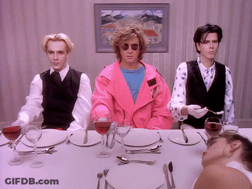 A Man In A Pink Jacket Sits At A Table With Plates And Glasses Of Wine GIF