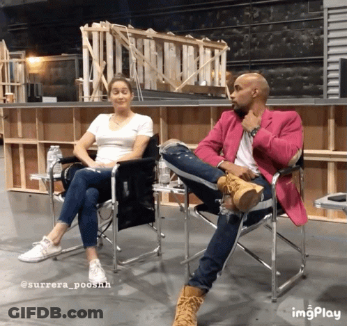 A Man In A Pink Jacket Sits Next To A Woman In A White Shirt And Jeans GIF