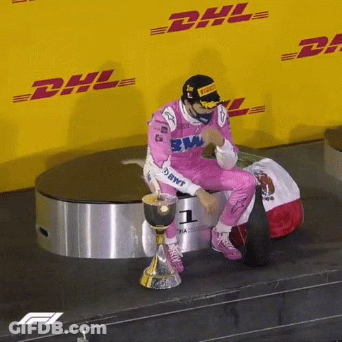 A Man In A Pink Racing Suit Is Sitting On A Podium With A Trophy In Front Of A Dhl Sign GIF
