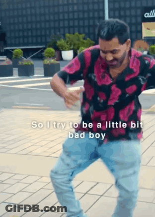 A Man In A Pink Shirt And Blue Jeans Is Dancing On A Brick Sidewalk . GIF