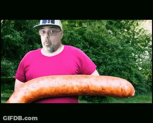 A Man In A Pink Shirt Holds A Very Large Sausage GIF