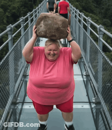 A Man In A Pink Shirt Is Carrying A Large Rock Over His Head GIF