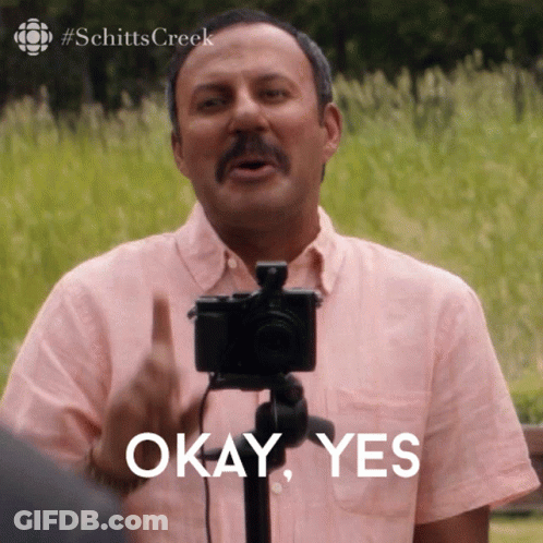 A Man In A Pink Shirt Is Holding A Camera And Says " Okay Yes " GIF