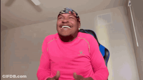 A Man In A Pink Shirt Is Holding A Game Controller And Laughing GIF